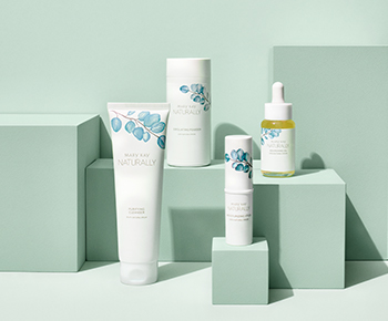 The Mary Kay Naturally products in white packaging with teal leaf illustrations on a green background