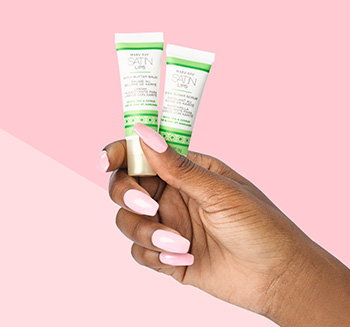 The Mary Kay Satin Lips Set is photographed in an African American model’s pink manicured hand in front of a two-toned pink background.