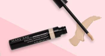 An open tube of Mary Kay Perfecting Concealer is photographed alongside its doe foot applicator and a product smear in front of a two-toned pink background.