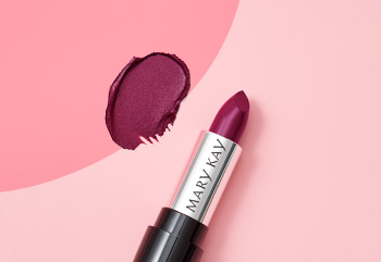 A berry colored Mary Kay lipstick is photographed with its cap off atop a two-toned pink background and alongside a product smear.