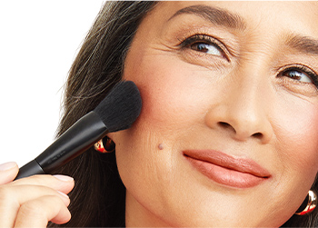 A mature Asian model applying blush to her cheeks with the Mary Kay Cheek Brush