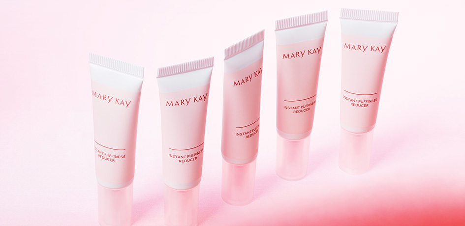 Several tubes of Instant Puffiness Reducer stand against a cloudy pink backdrop.