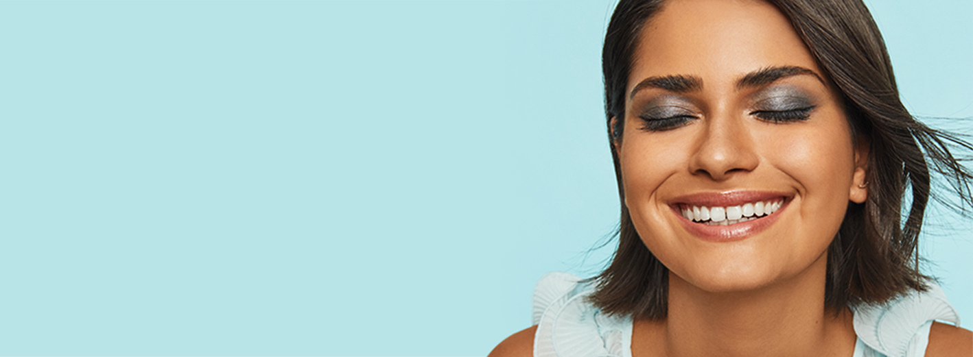 Smiling model with closed eyes wearing Pop of Color Mary Kay makeup artist look against blue background.