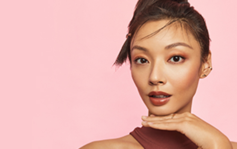 Une femme souriante d’origine asiatique, à la peau rayonnante, porte un maquillage minimaliste.