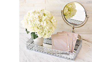 Three packages of TimeWise Repair Lifting Bio-Cellulose Masks are arranged in a silver spa tray next to a vase of white flowers and a mirror.