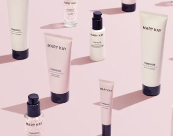 Four Mary Kay products from the new TimeWise Miracle Set 3D skin care regimen are shown in pink and grey packaging in front of glass beakers filled with pink liquid. The set includes the 4-in-1 Cleanser, the Day Cream SPF 30, the Night Cream and the Eye Cream.