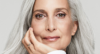 A mature white woman with gray hair and beautiful skin resting her chin on her hand