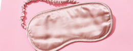 Light pink silky sleeping eye mask laying on a darker pink background