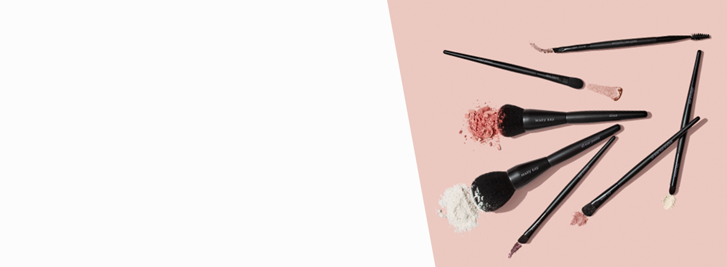 Un mélange de pinceaux pour le maquillage Mary Kay avec des frottis de produits sur un arrière-plan rose pâle.