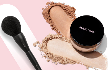 A jar of Mary Kay Silky Setting Powder sits atop smears of beige face powder and next to an all-over powder makeup brush in front of a pink and white background