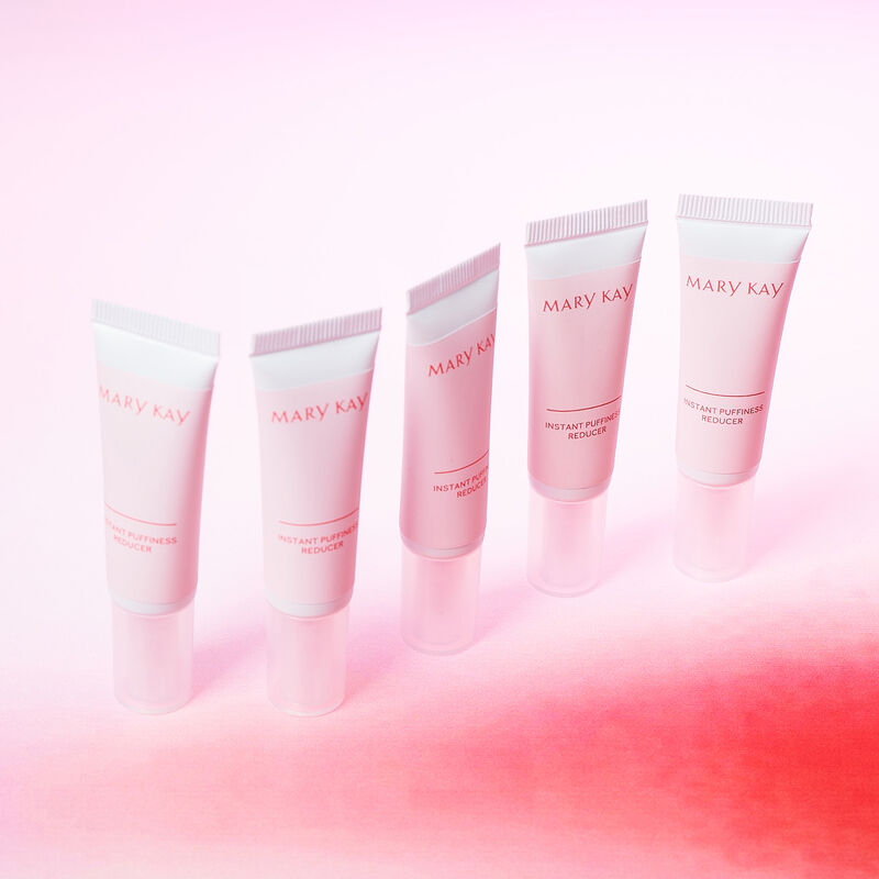 Five tubes of Mary Kay Instant Puffiness Reducer against pink gradient background
