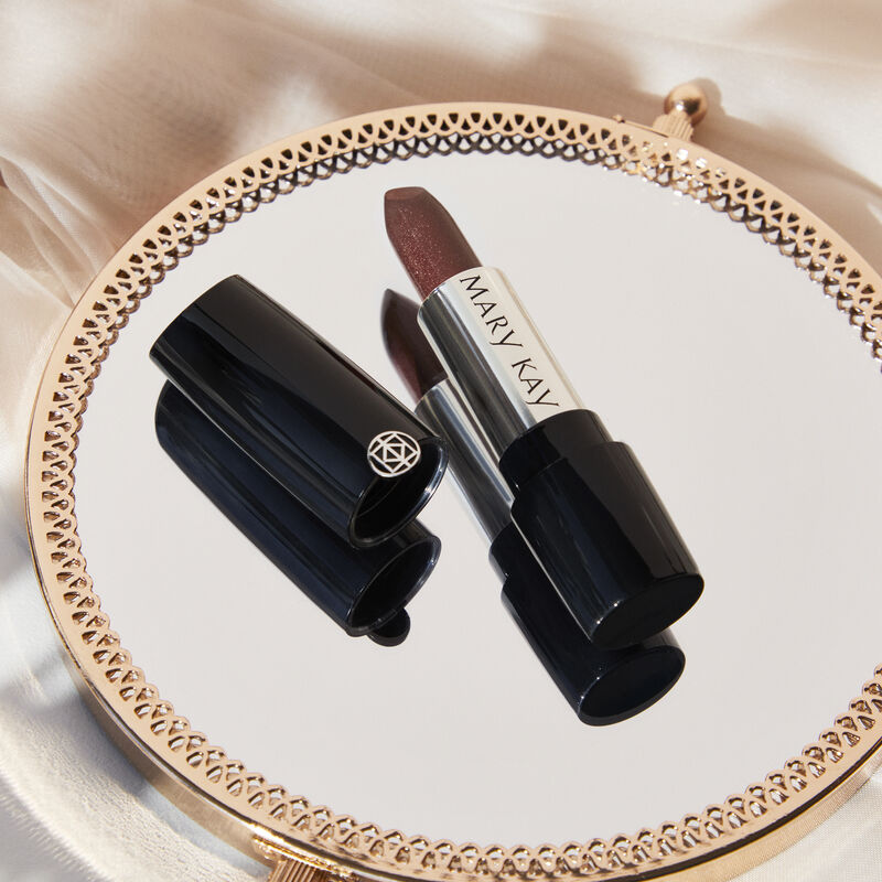 Uncapped tube of Mary Kay Gel SemiShine Lipstick in Downtown Brown on gold mirror