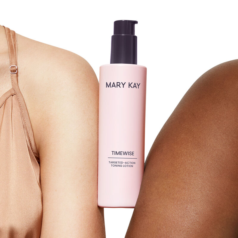 Bottle of TimeWise TargetedAction Toning Lotion being held between medium skinned and deep skinned shoulders against light pink background
