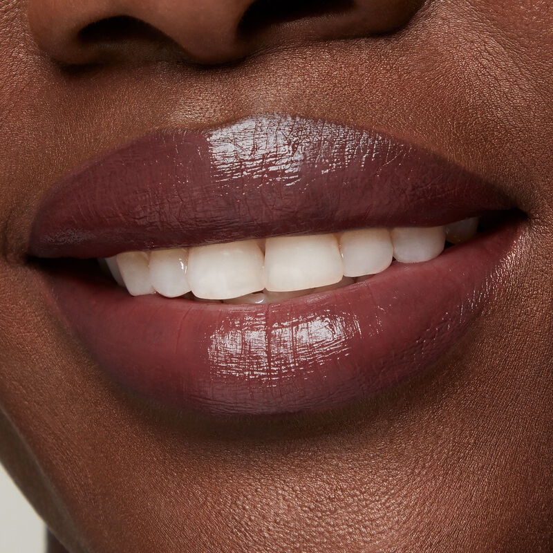 Close up of deep skinned model&rsquo;s smiling lips wearing Mary Kay Supreme Hydrating Lipstick in shade Toasted Plum.
