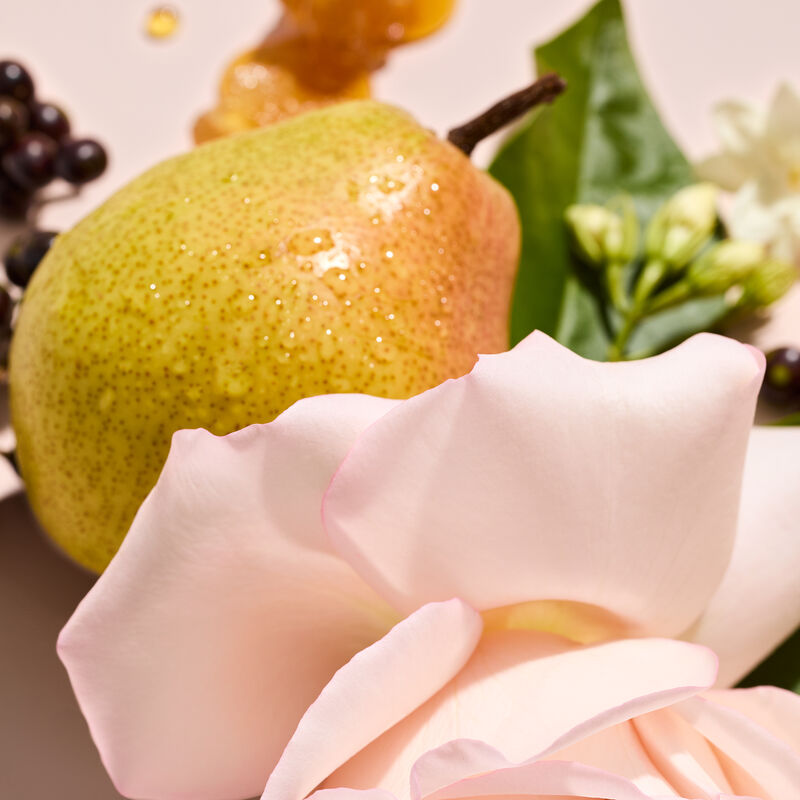 A juicy pear rose petals amber jasmine and cassis bud appear together on a table