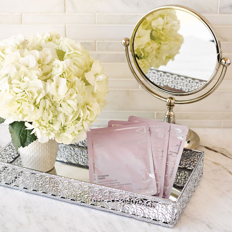 Trois bo&icirc;tes du Masque bio-cellulose lifting TimeWise Repair de Mary Kay agenc&eacute;es sur un plateau d&eacute;coratif avec un miroir et des fleurs.