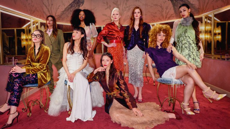 Group of nine women in vibrant wardrobe posing together in a powder room.