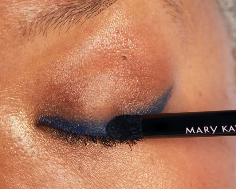 Close-up of model smudging blue eyeliner with a makeup brush