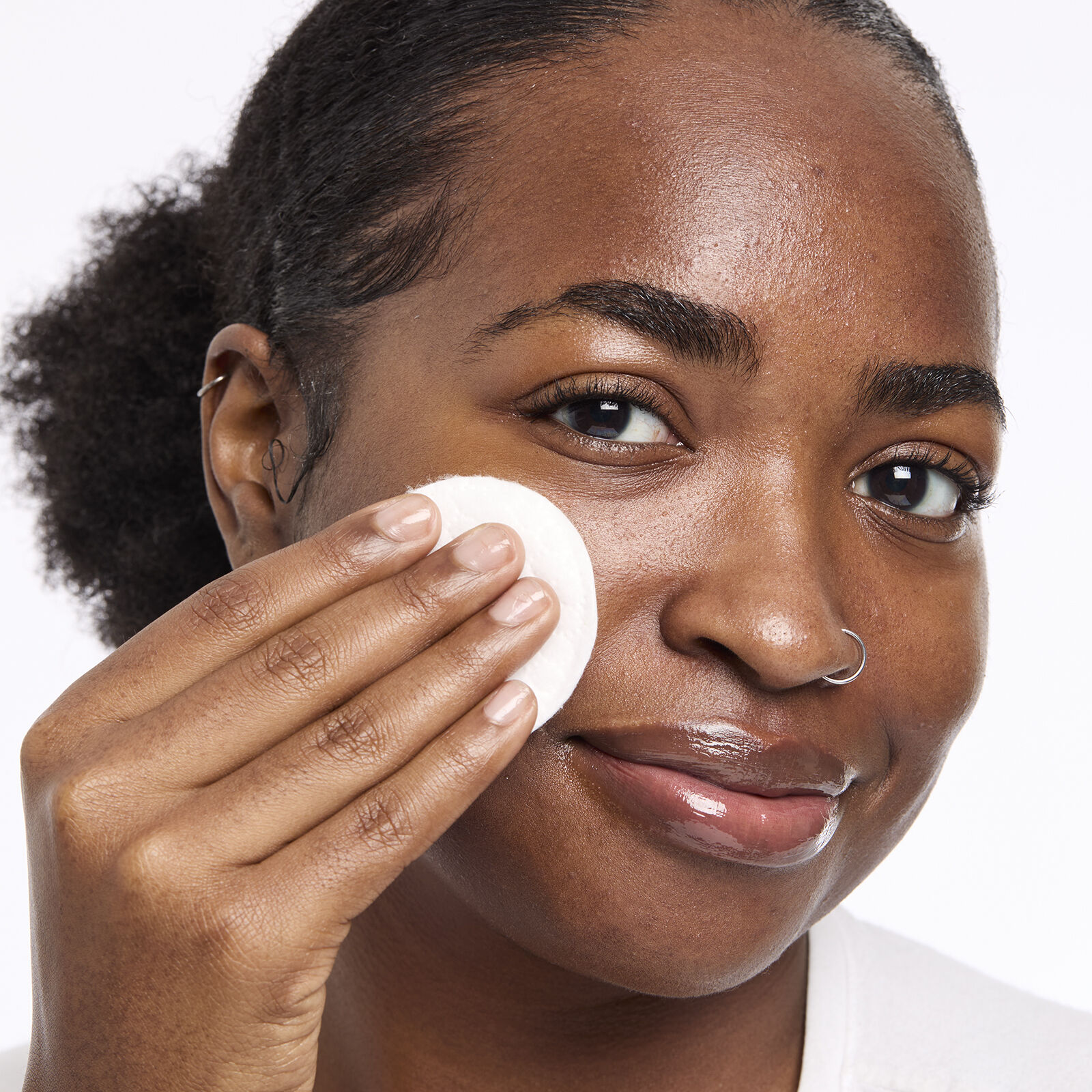 A women using a cotton pad to apply product to her face, with natural textured hair pulled back