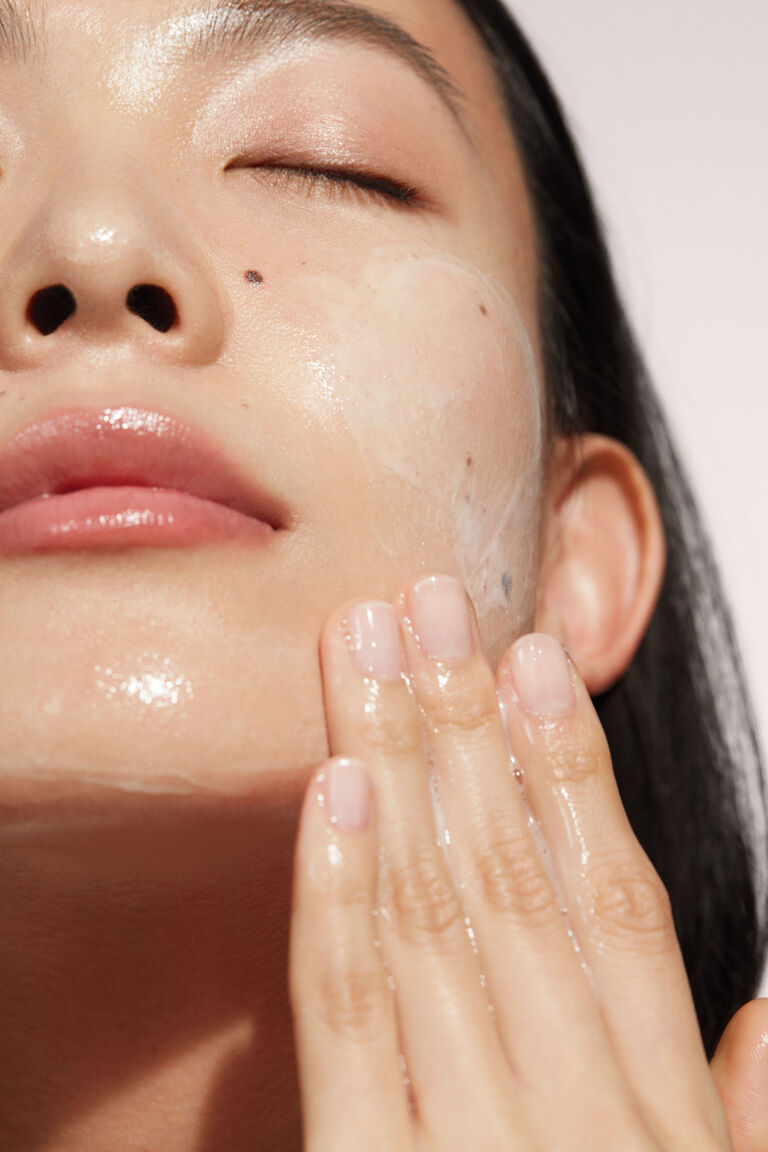 A close up of a woman applying Mary Kay Timewise Miracle Set cleanser.
