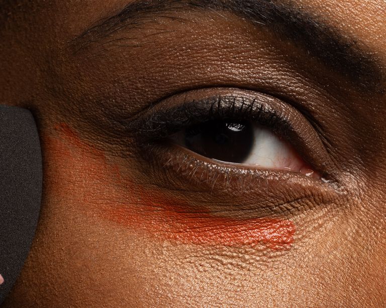 Close-up of a model applying undereye corrector with a makeup sponge