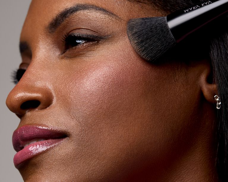 Model applying blush to the top of her cheek with a makeup brush