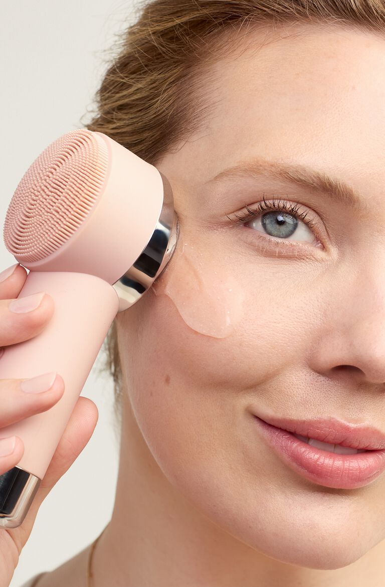 Close-up of a person&rsquo;s face with a skincare device applied to the cheek, spreading a white facial cream across the skin.