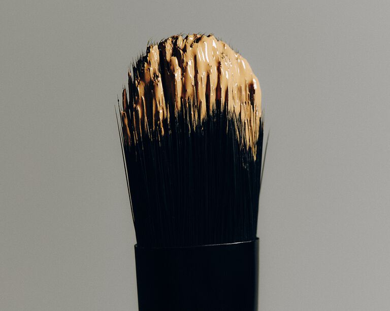 Makeup brush covered in a light shade of concealer