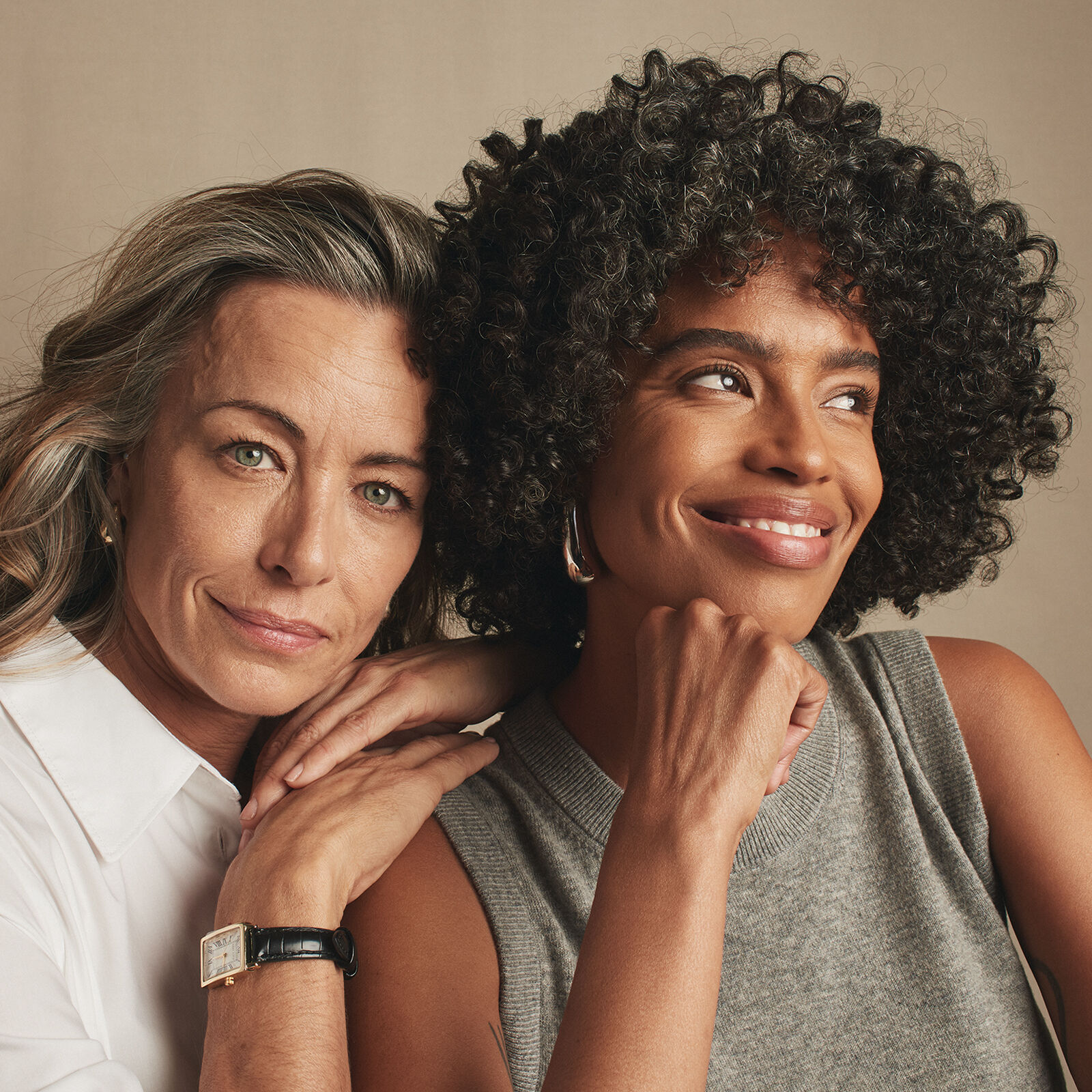 Deux femmes assises ensemble dont l&rsquo;une porte une chemise blanche et l&rsquo;autre un haut gris sans manche sont pench&eacute;es l&eacute;g&egrave;rement l&rsquo;une vers l&rsquo;autre.