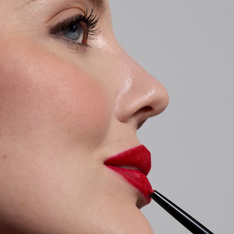 Side profile of a model applying red lipliner to her lips 