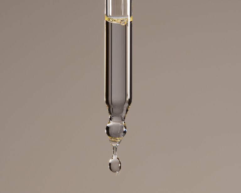 Close-up of a dropper dispensing a bead of oil