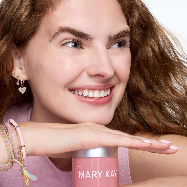 Smiling woman resting her hand and head on jar of Mary Kay Collagen Moisturizing Gel