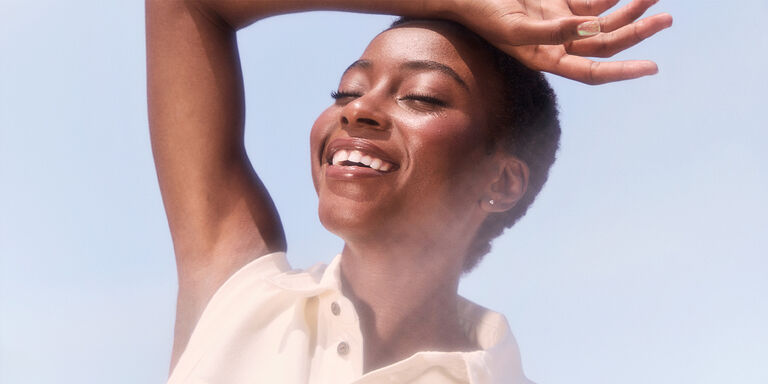 Model smiling under a blue sky and sun