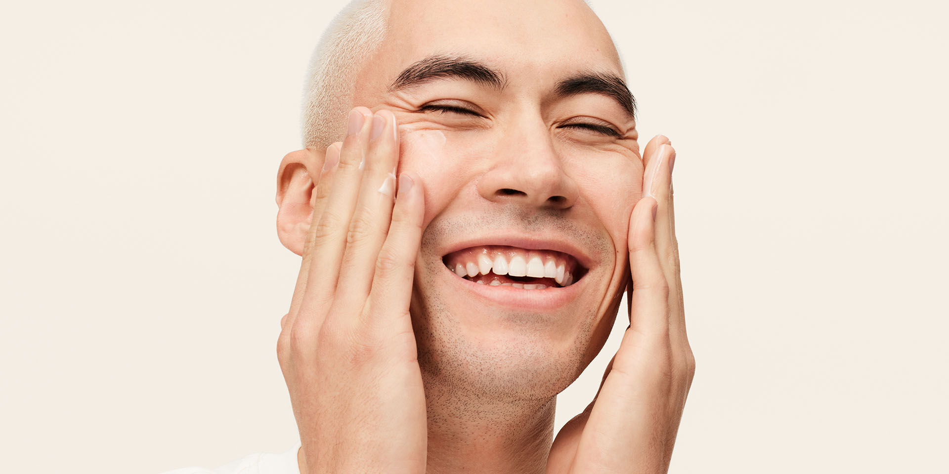 Male model smiling and applying MK Men Moisturizer to his face