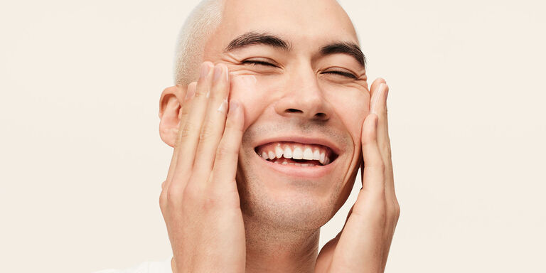 Male model smiling and applying MK Men Moisturizer to his face