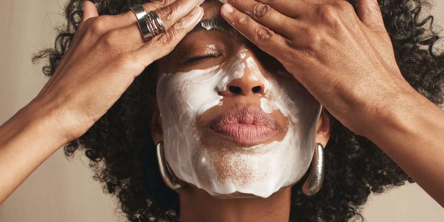 Mannequin de teint fonc&eacute; au cheveux noirs fris&eacute;s nettoyant son visage, bouche et yeux ferm&eacute;s.