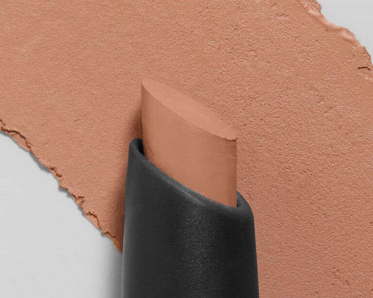 Tip of a light brown eye shadow stick in front of the product swatch