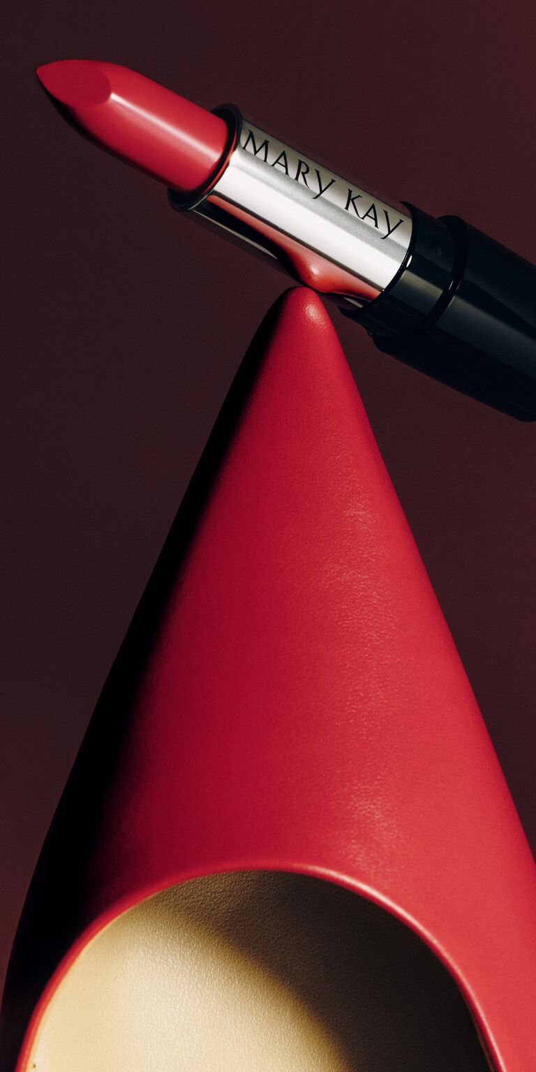 Close-up of a pointed red heel with a red lipstick balanced on its tip
