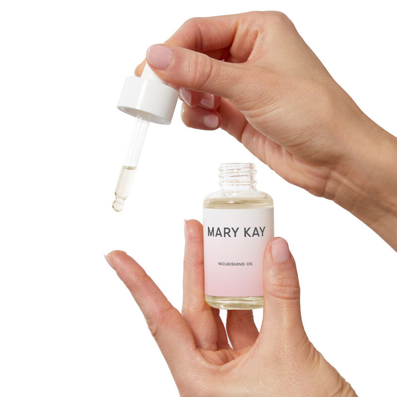 Fair-skinned hands holding bottle of Mary Kay Nourishing Oil and dispensing it with included dropper.