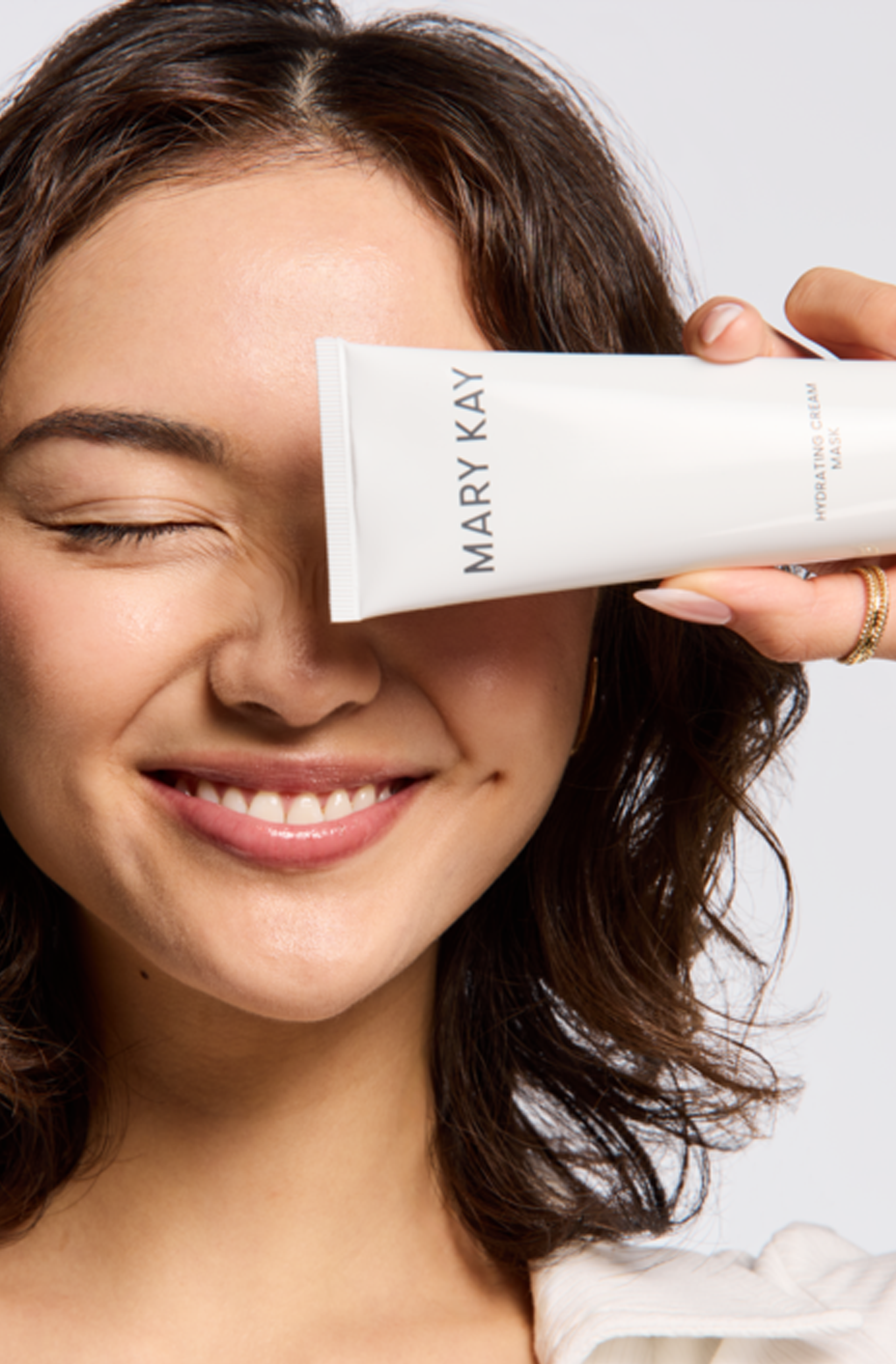 A person holds a tube of Mary Kay Cleanser over their eye while smiling