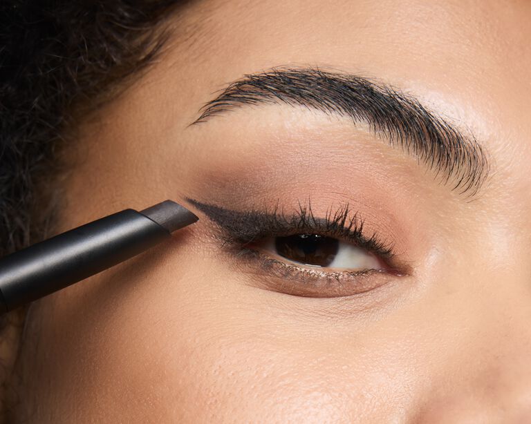 Model using a matte eyeshadow stick along the lash line as eyeliner