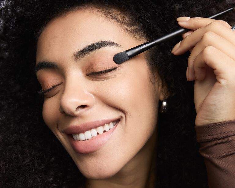 Model applying eyeshadow to her eyelid using a brush